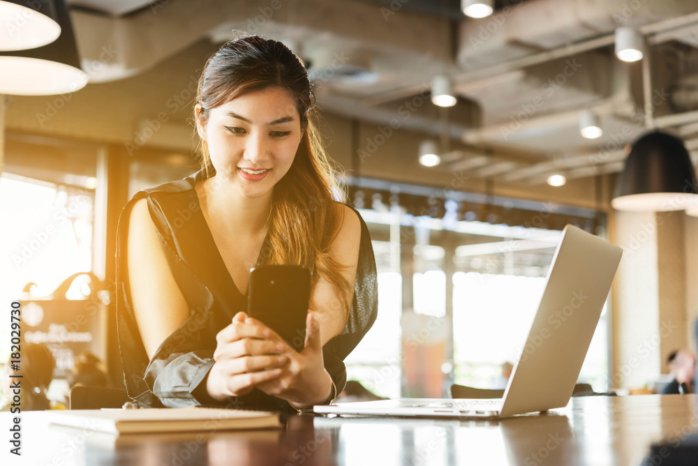 Beautiful asian woman in black dress working with smartphone and laptop in coffeeshop