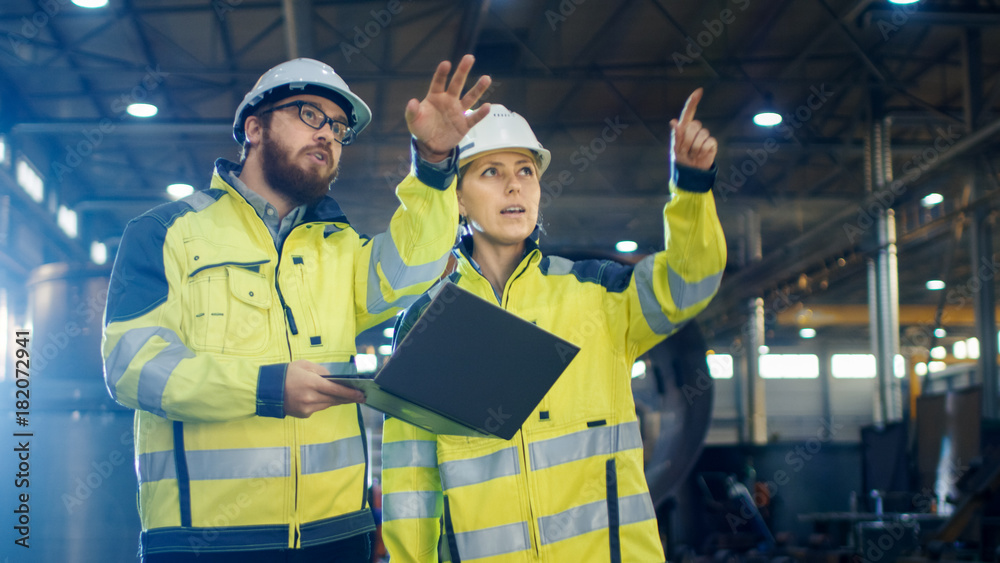 Male and Female Industrial Engineers Having Discussion and Use Laptop While Walking Through Heavy In