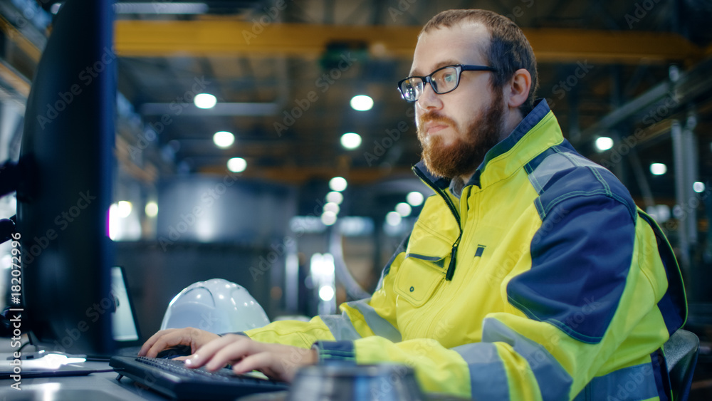 Industrial Engineer Works at Workspace on a Personal Computer.  He Wears  Safety Jacket and Works in