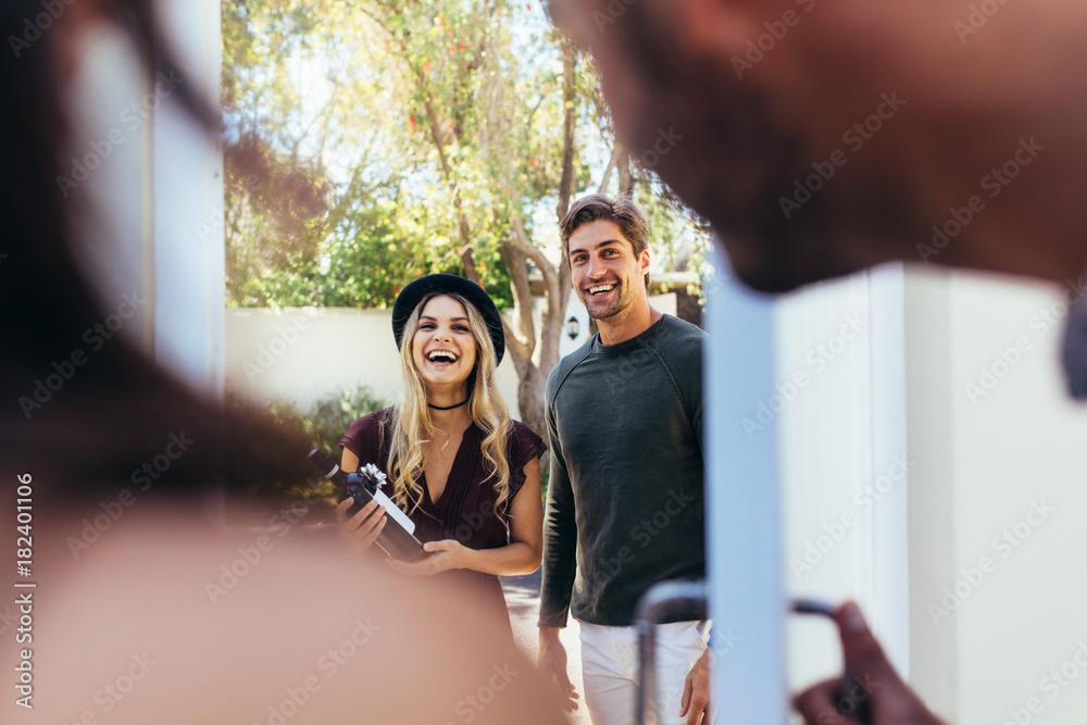 Smiling young couple at entrance door with wine bottle