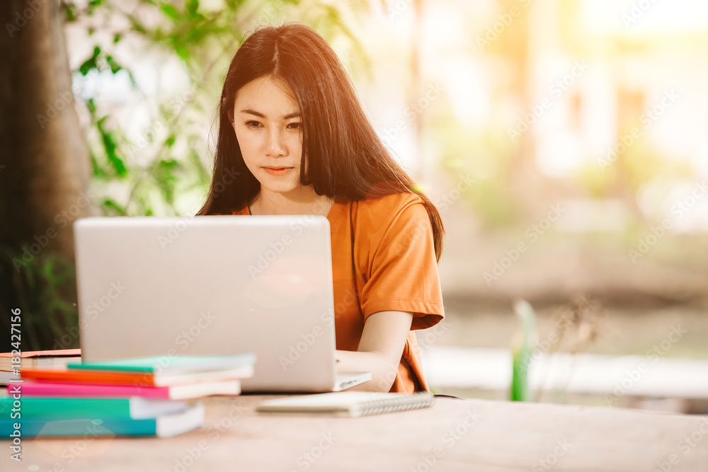 一个年轻或十几岁的亚洲女学生在大学里微笑着看书，看着平板电脑