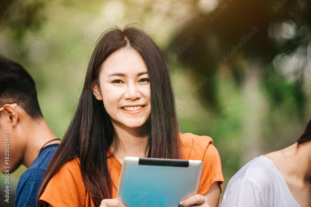 一个年轻或十几岁的亚洲女学生在大学里微笑着看书，看着平板电脑