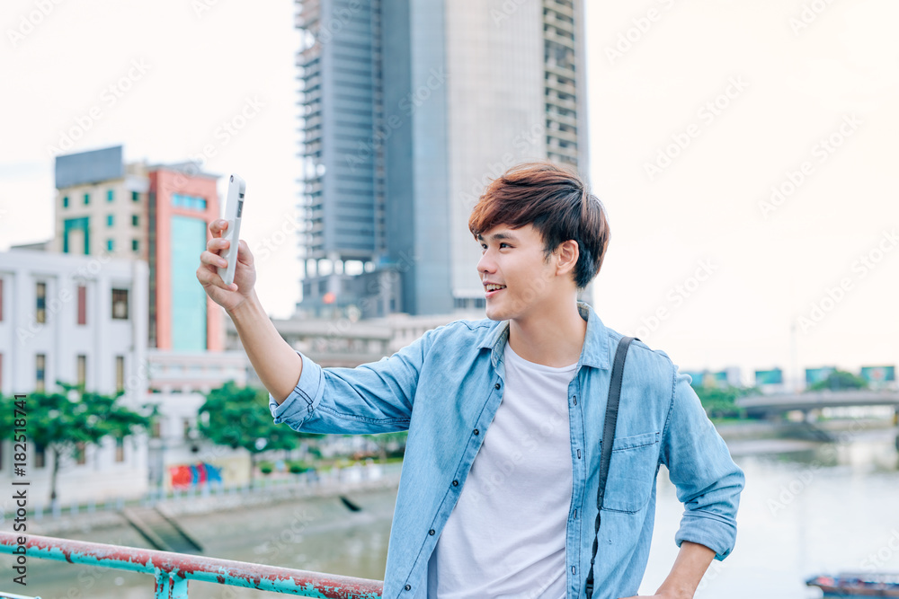 Young asian man tourist taking selfie photo using smartphone outdoor in the city