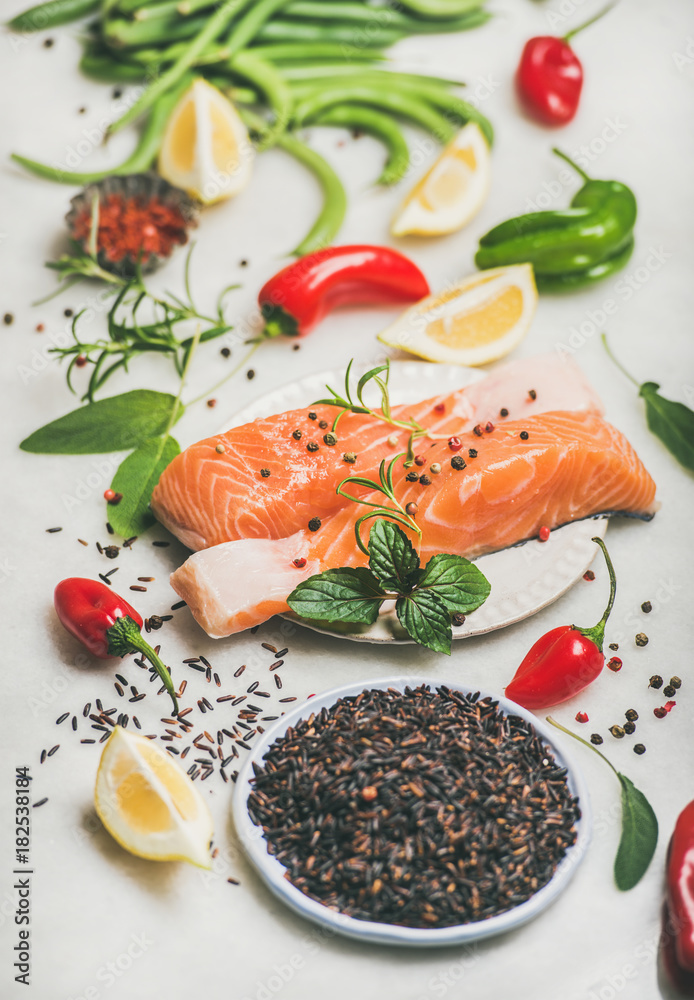 Raw uncooked salmon fish fillet steaks with vegetables, greens, rice and spices over grey marble bac