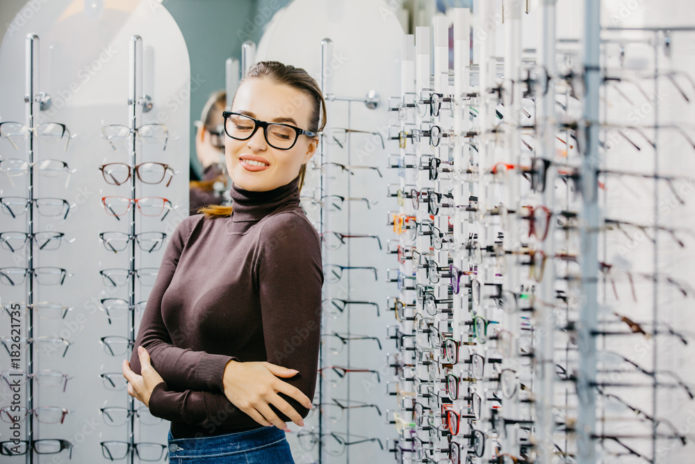 Ophthalmology. Young woman is choosing a glasses in optician store. Eyesight correction.