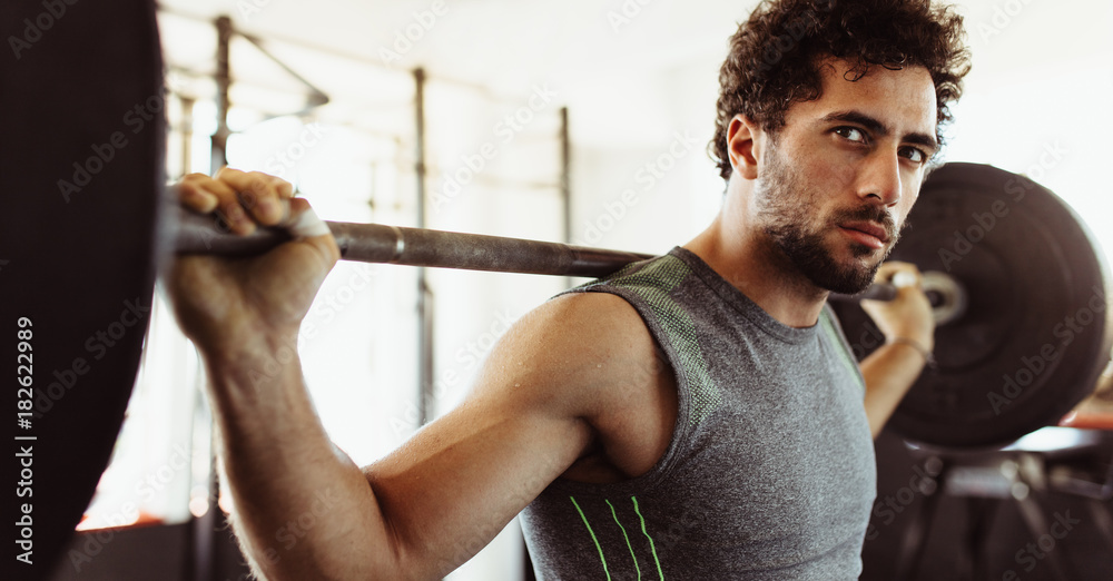 Confident young man exercising with barbell