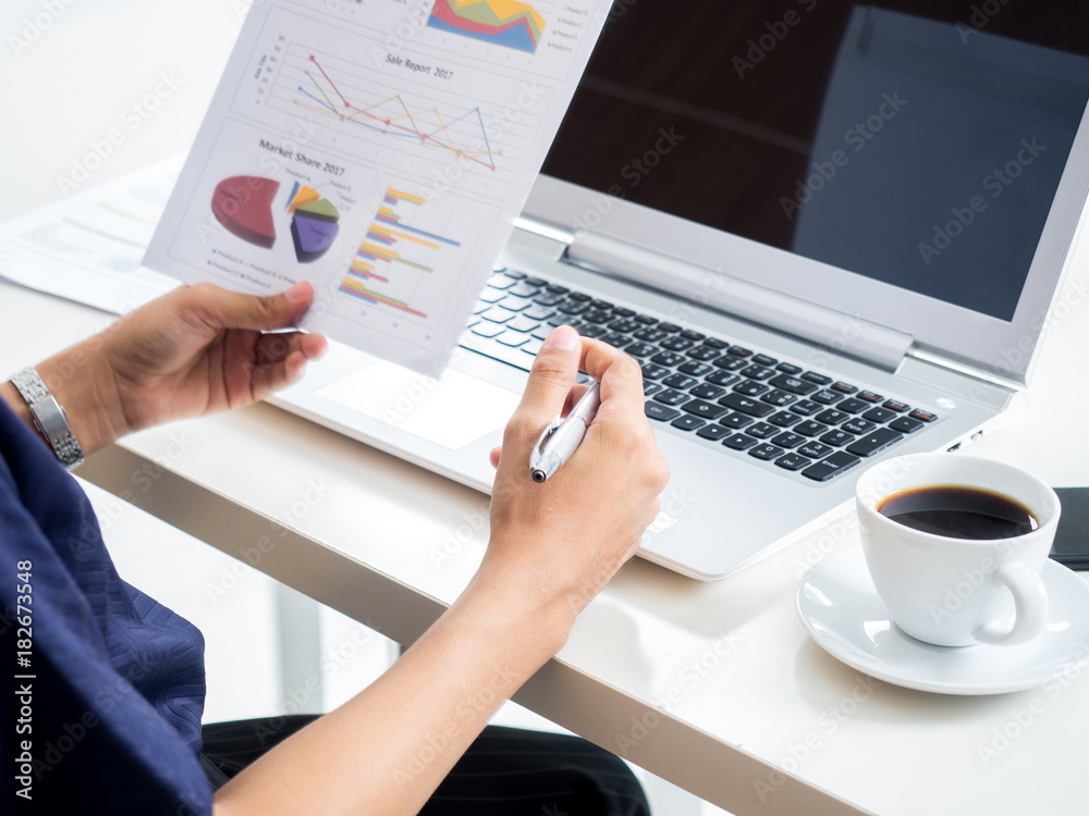 Businesswoman working in office, reading a financial report/documents using laptop and drink cofee a