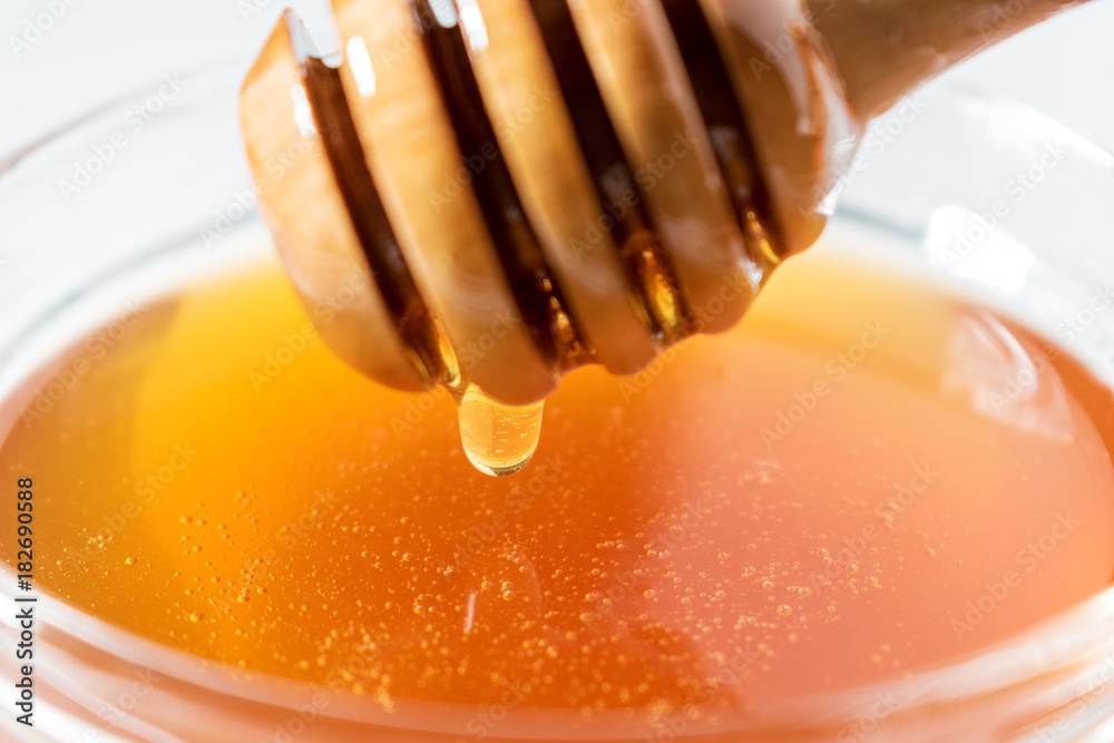 Honey dripping from honey dipper on white background. Thick honey dipping from the wooden honey spoo