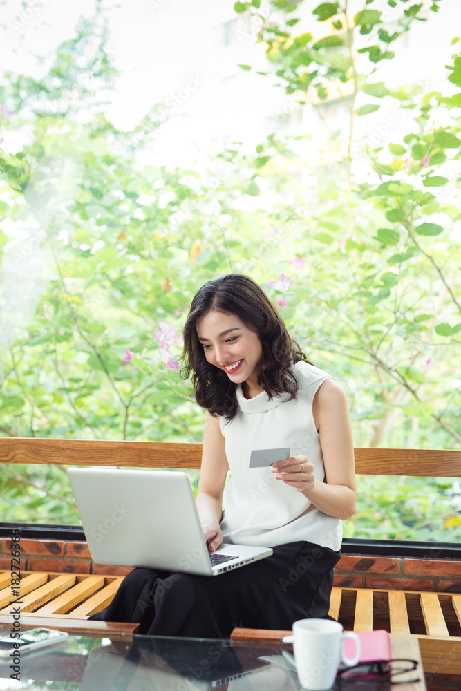 Asian woman shopping online while sitting near window in creative office or cafe