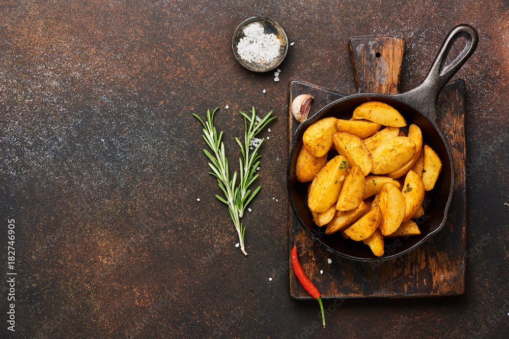 Roast potato with salt and spices in pan on wooden board on brown background with copy space. Top vi