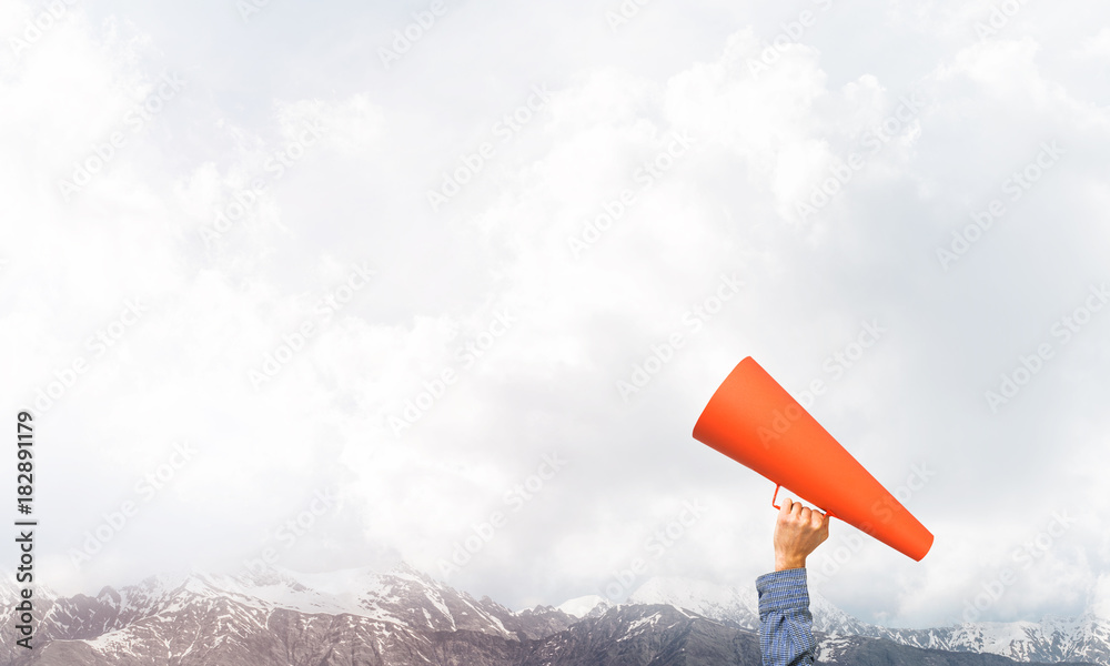 Hand of man holding paper trumpet against natural landscape background