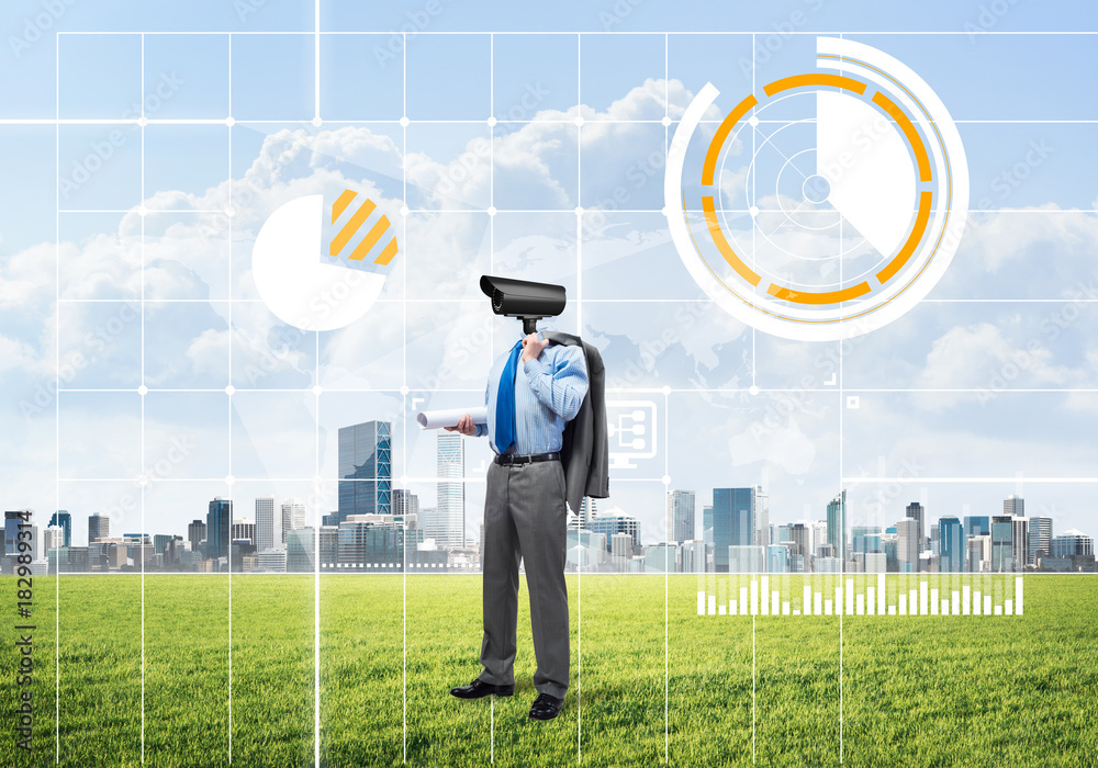 Camera headed man standing on green grass against modern cityscape