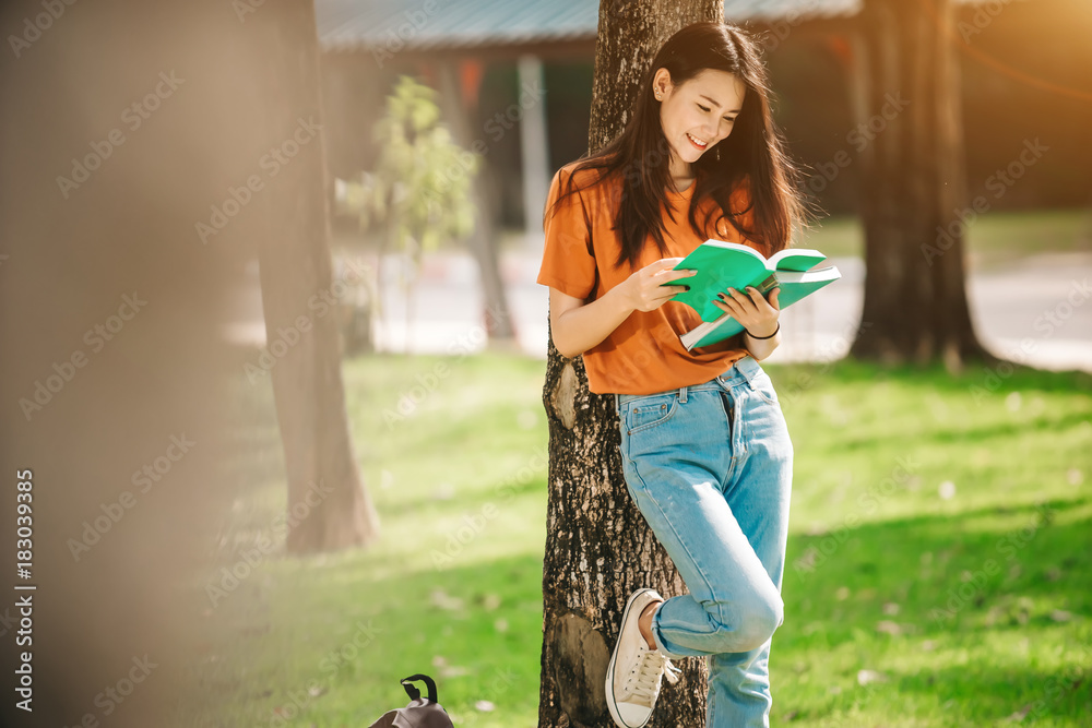 A young or teen asian girl student in university smiling and reading the book and look at the tablet