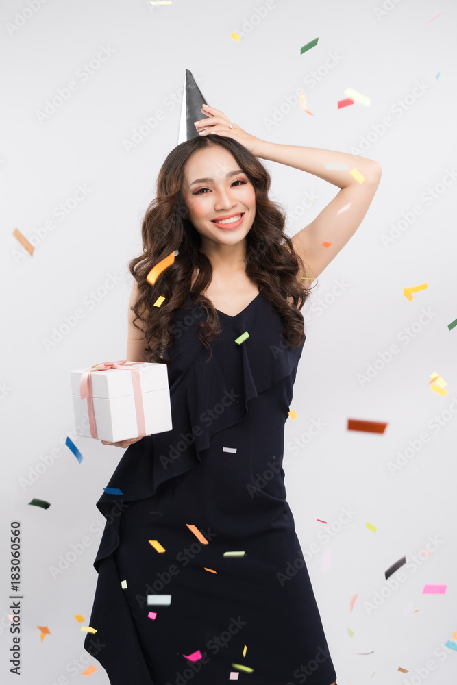 Portrait of asian woman in birthday hat and confetti on white background. Celebration and party.