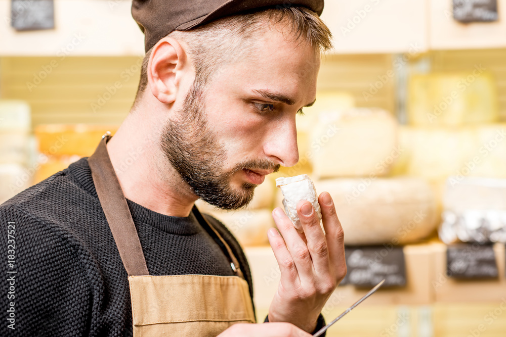 Portrait of a handsome cheese seller in uniform smelling young cheese in front of the store showcase