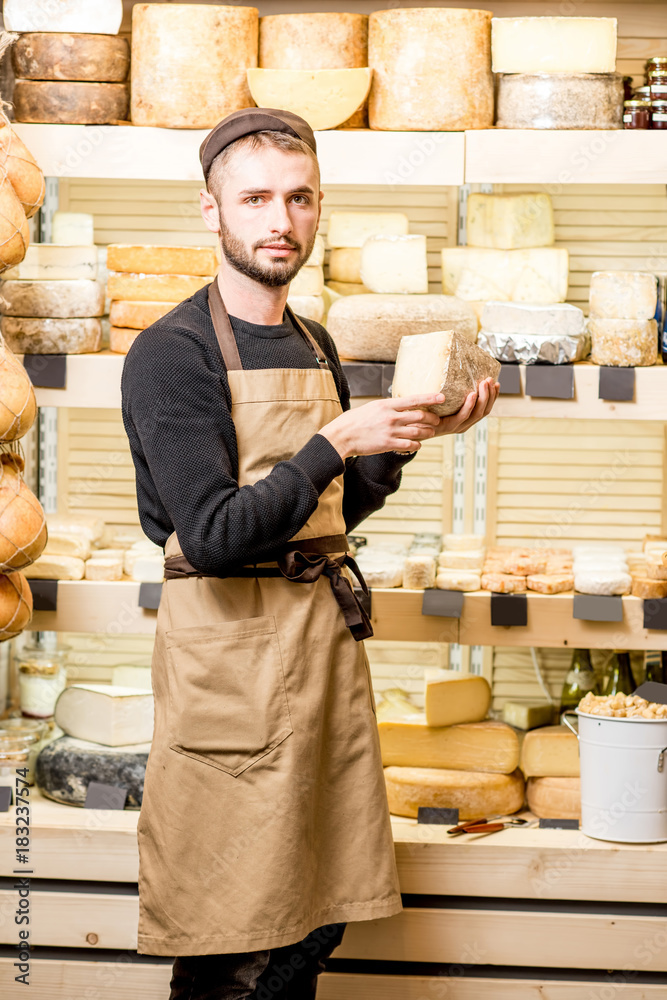 Portrait of a handsome cheese seller in uniform standing in front of the store showcase full of diff