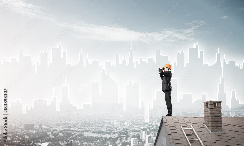 Engineer man standing on roof and looking in binoculars. Mixed m