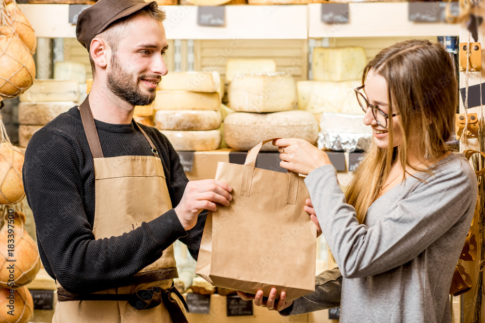 Salesman packing shopping bag with goods and giving to the woman customer at the cheese shop