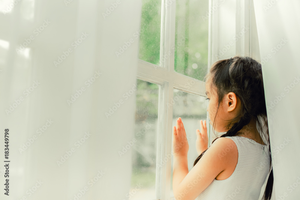 Sad child, Little girl looking the rain falling through a window at home