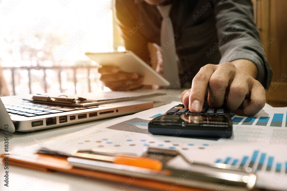 businessman hand working with finances about cost and calculator and laptop with tablet on withe des