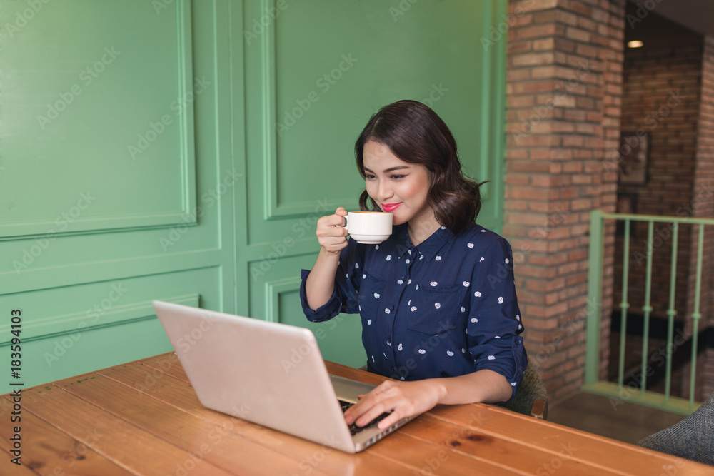 Beautiful cute asian young businesswoman in the cafe, using laptop and drinking coffee smiling