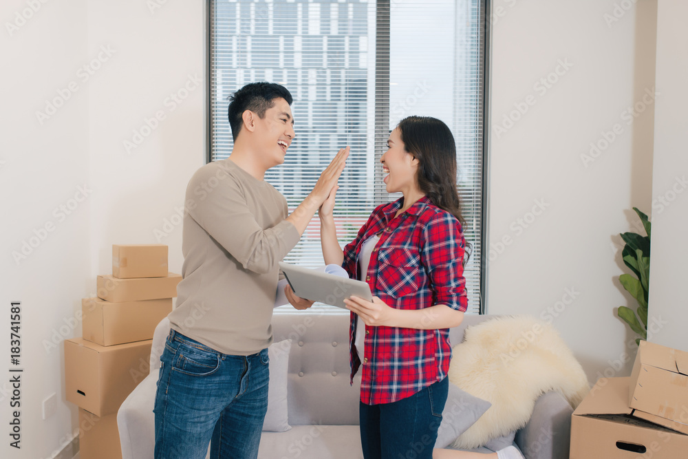 Concept young couple moving house. Beautiful young couple giving high five and smiling while standin