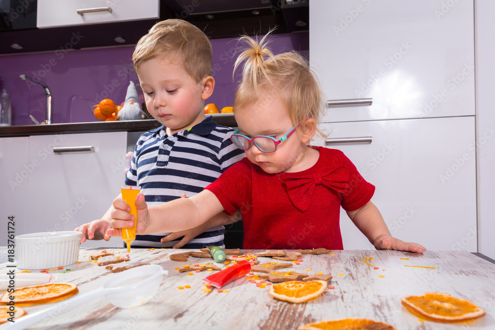 Cute little boy and girl twins decorating Christmas cookies in the kitchen