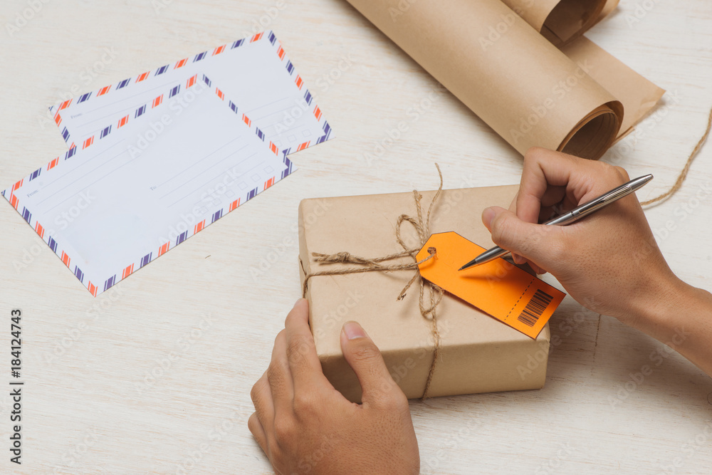 Male hand writing on luggage tag on brown paper parcel