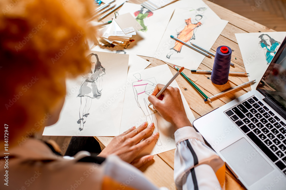 Fasion designer sketching clothes drawings at the table with tailoring tools and laptop