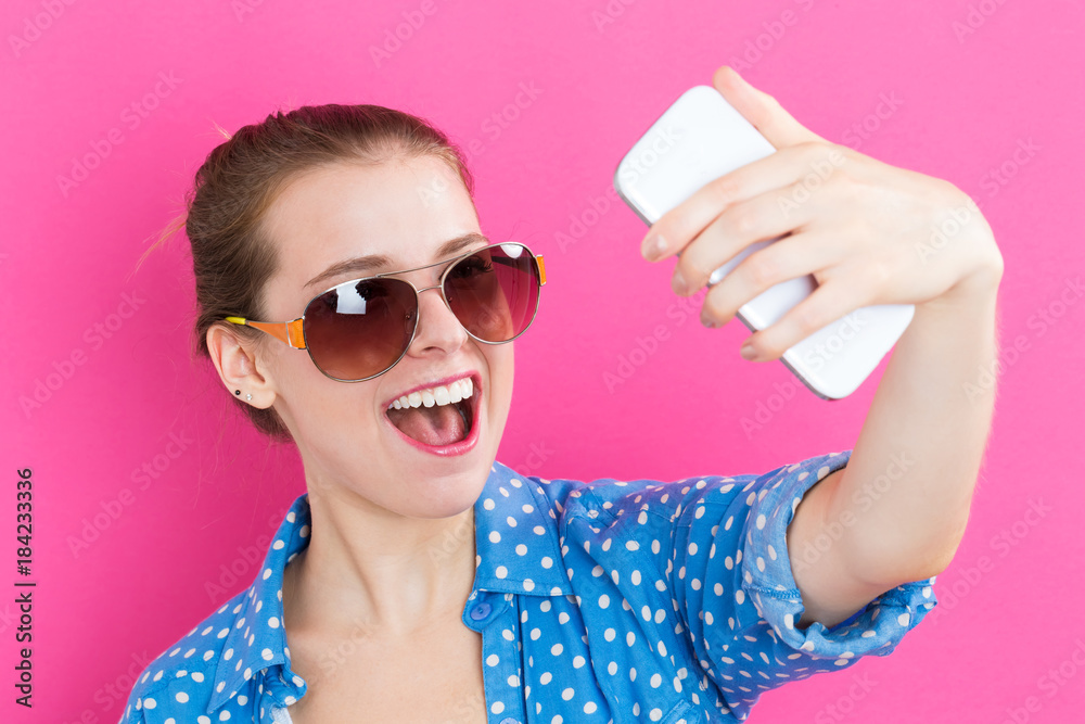 Young woman taking a selfie on a pink background