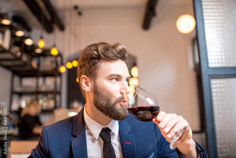 Handsome businessman dressed in the suit drinking red wine sitting at the restaurant