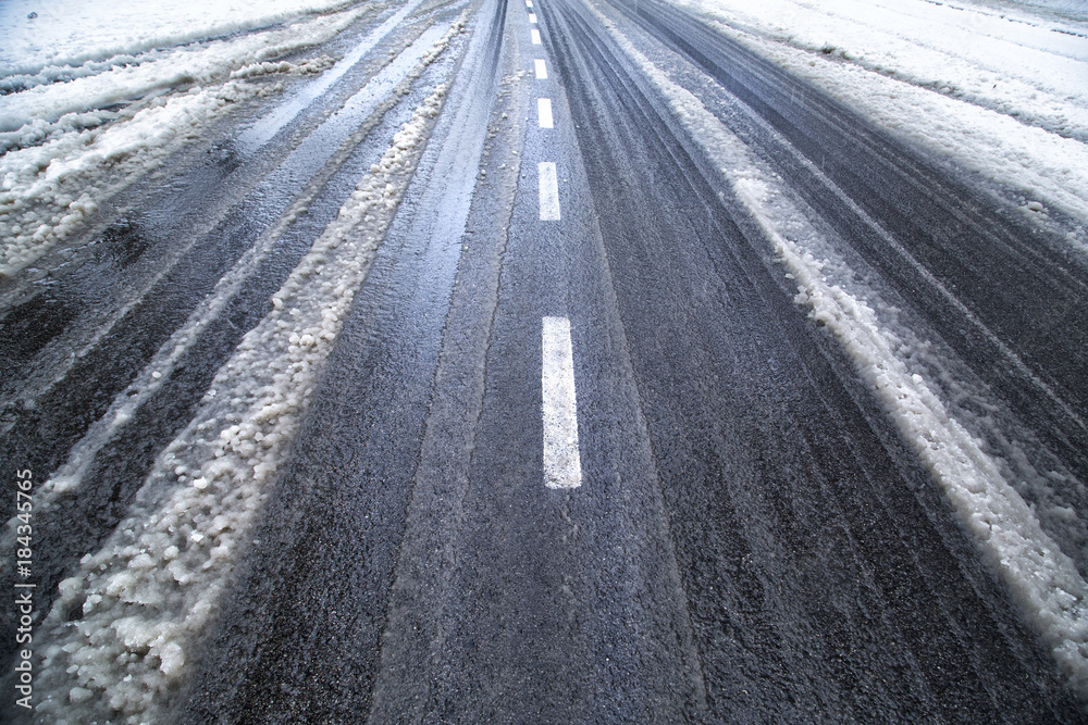 雪地湿滑的冬季沥青路面，有轮胎痕迹。