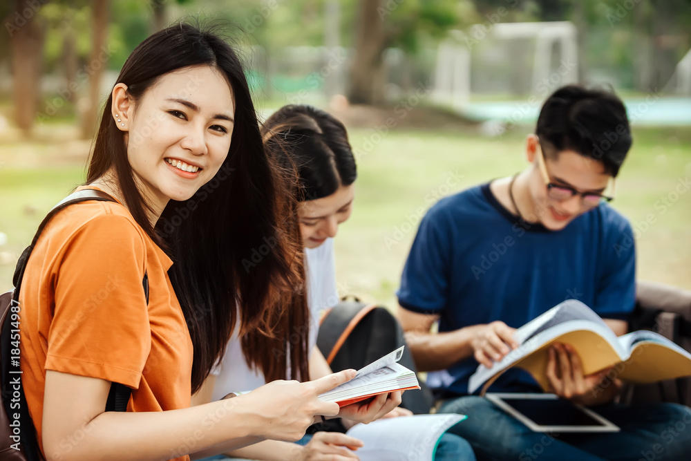 一群年轻或十几岁的亚洲学生在大学里微笑着读着书，看着ta