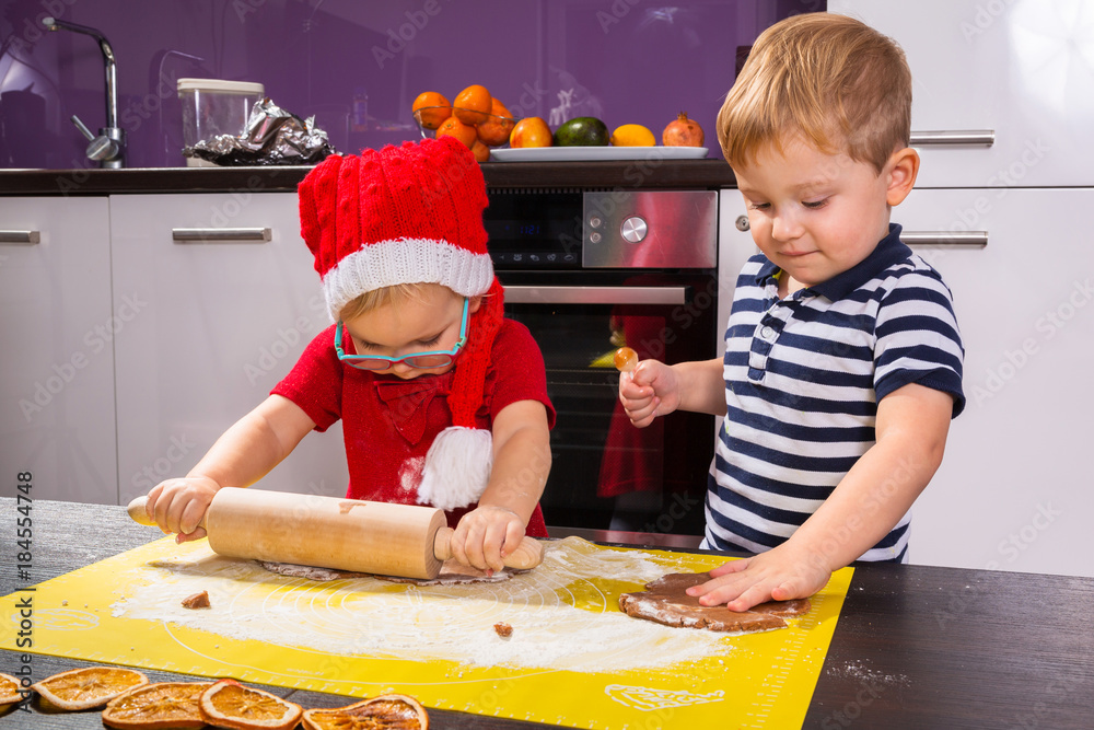 Cute little boy and girl twins preparing Christmas cookies in the kitchen