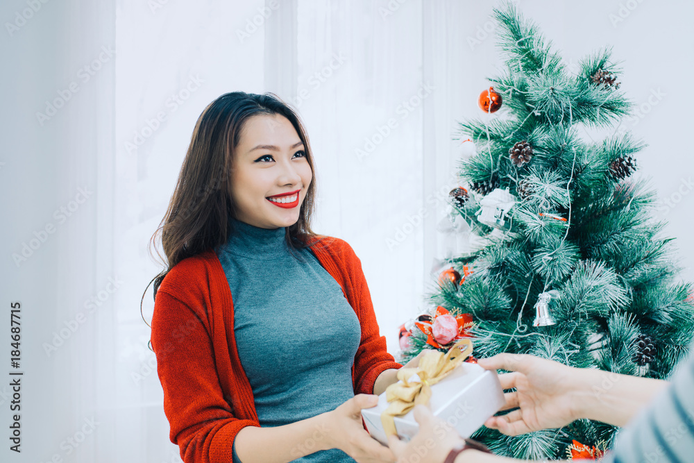 圣诞亚洲情侣。一个英俊的男人在家里给她的女朋友/妻子送礼物庆祝新年