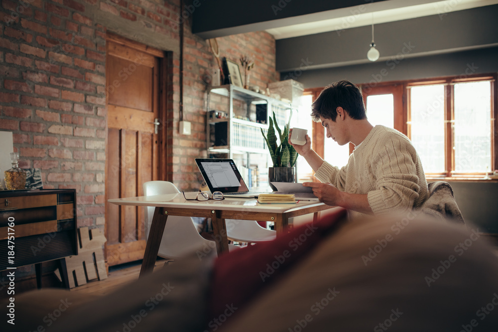 Young man sitting at table reading book and having coffee