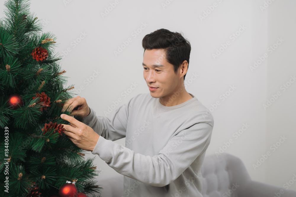 圣诞节。一名亚洲男子站在家里的新圣诞树上庆祝新年。