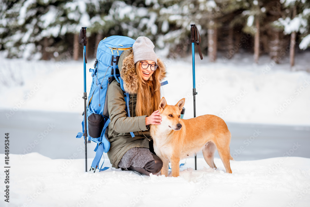 一名妇女在冬季徒步旅行中休息，在湖边的雪山上抚摸她的狗