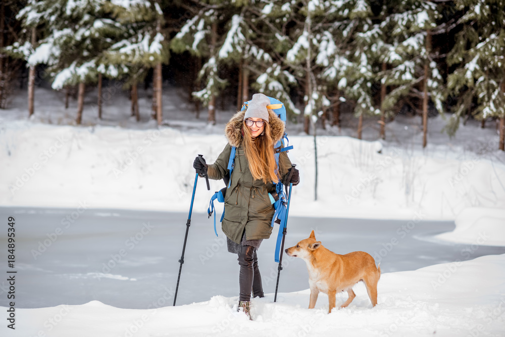 年轻女子带着狗在结冰的湖泊和白雪皑皑的森林附近徒步旅行