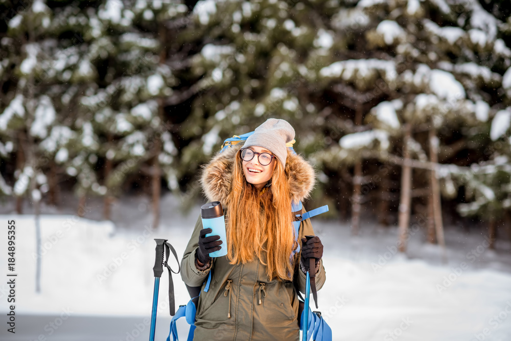 一个穿着冬装的女人在雪地里背着背包、跟踪棒和保温瓶徒步旅行的肖像