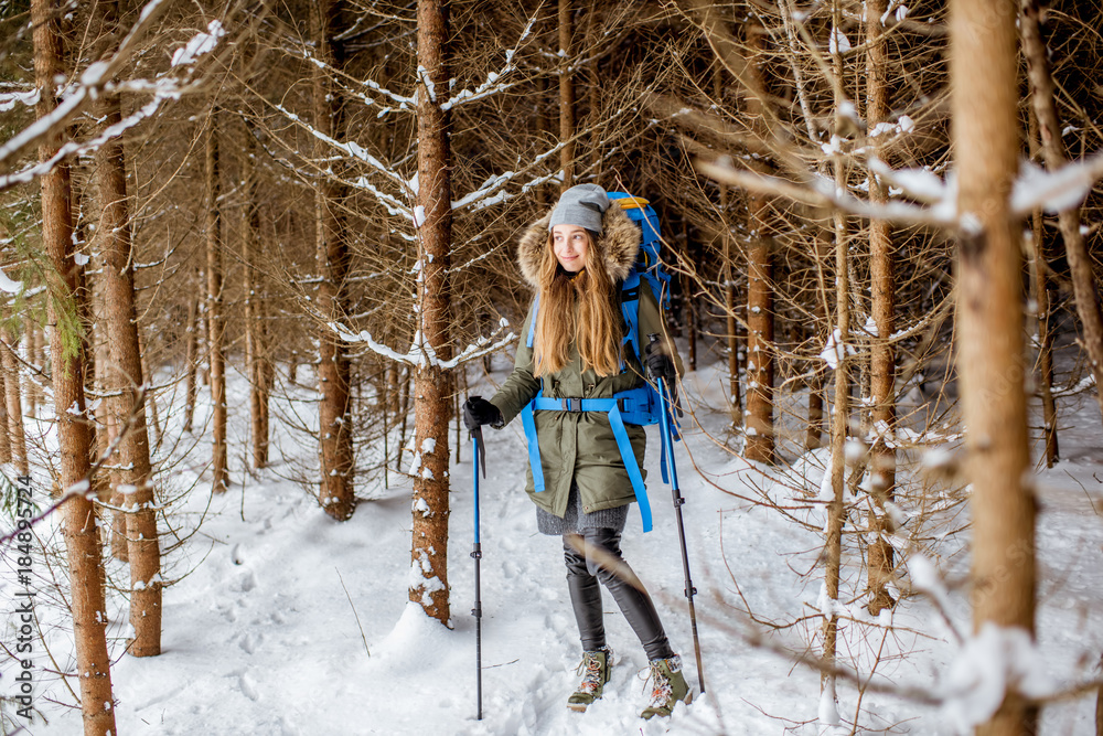 穿着冬装的女人背着背包和追踪棒在白雪皑皑的冷杉林中徒步旅行