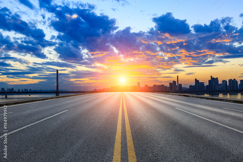 Empty asphalt road and city skyline at sunset