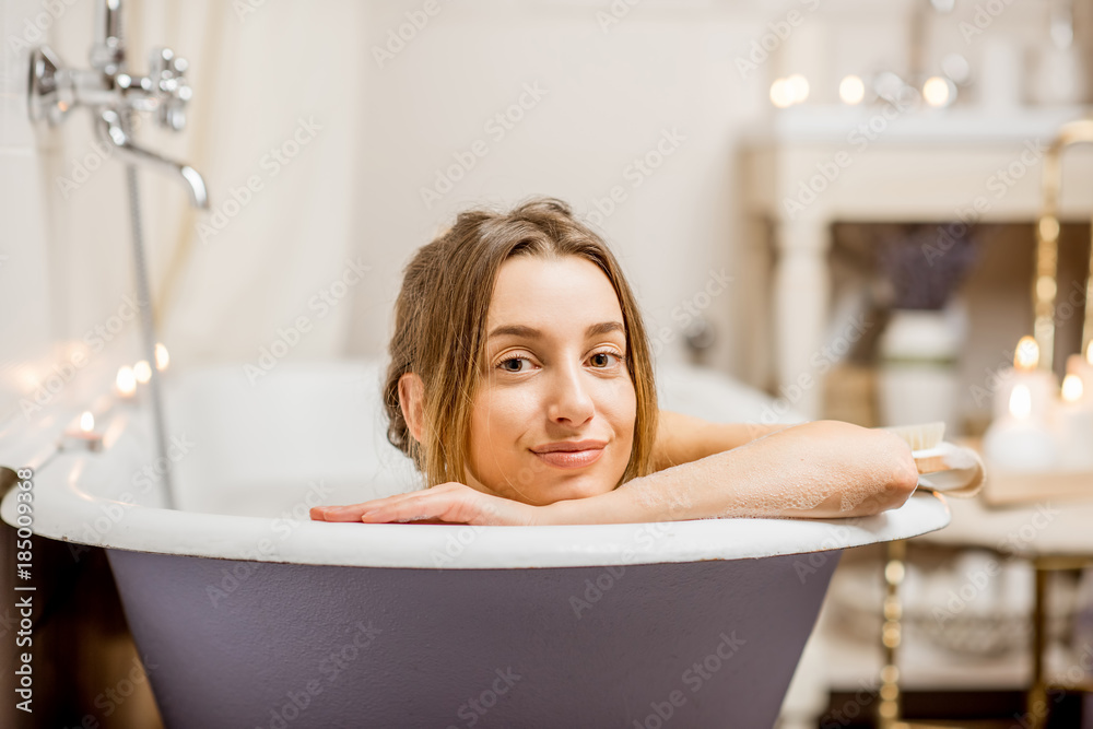 Portrait of a beautiful woman lying in the retro bath of the vintage bathroom decorated with candles