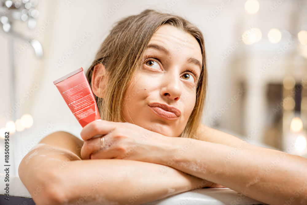 Close-up portrait of a pretty woman holding facial cream tube lying in the retro bathroom