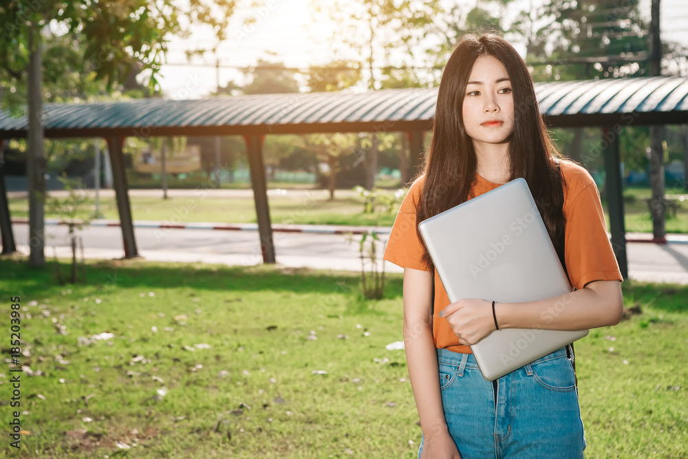 一个年轻或十几岁的亚洲女学生在大学里，暑假里拿着笔记本电脑