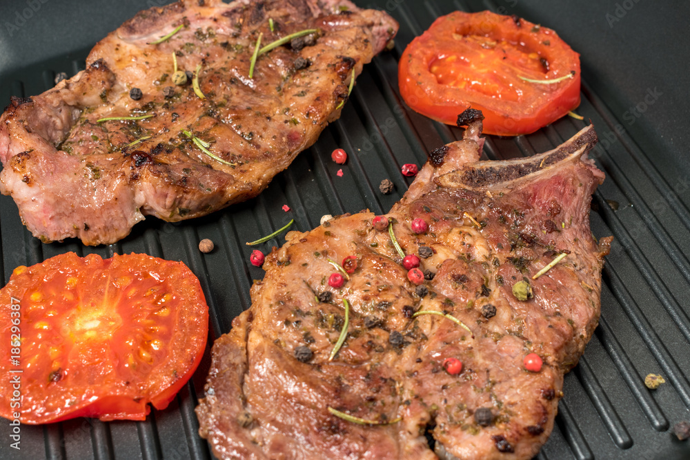 Grilled steak on grill pan with tomatoes on dark background