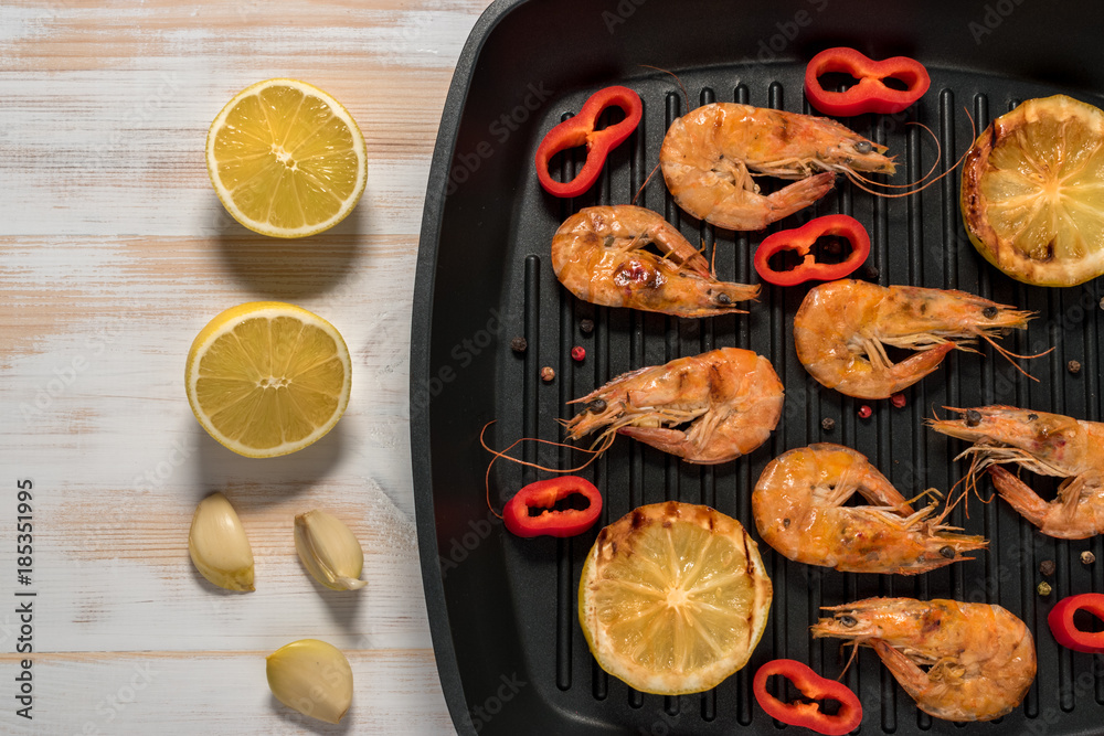 Grilled shrimps on a grill frying pan with lemon, paprika, spices and herbs. Wooden background.