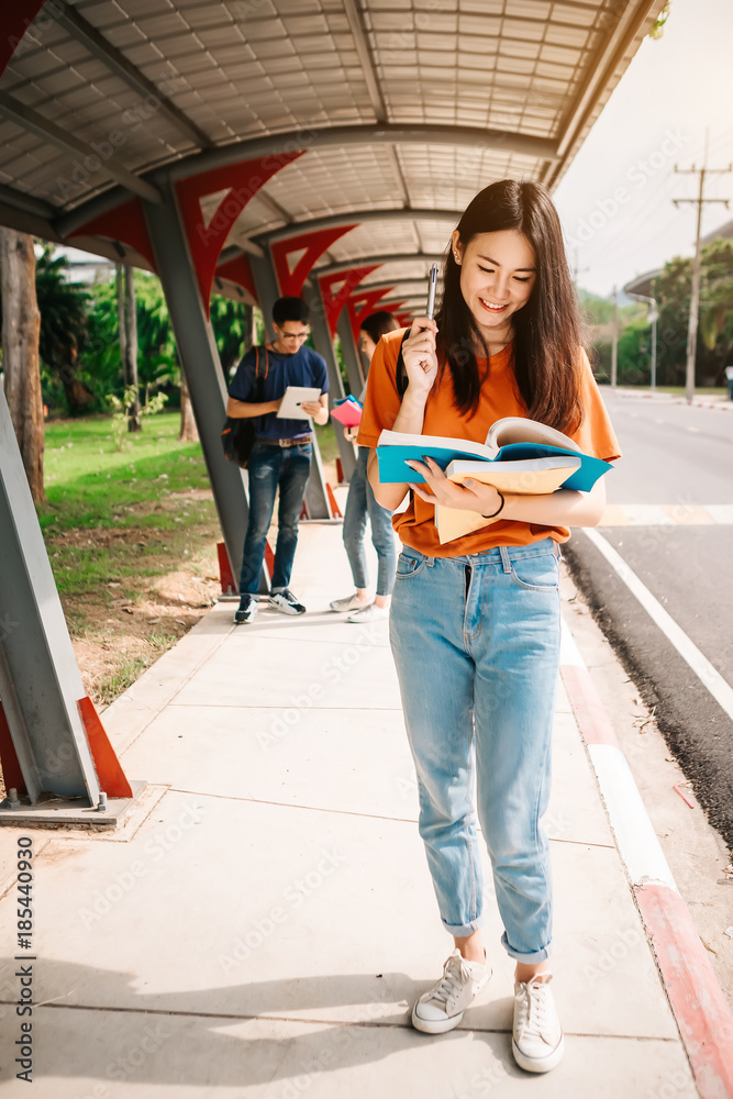 一群年轻或十几岁的亚洲学生在大学里微笑着读着书，看着ta