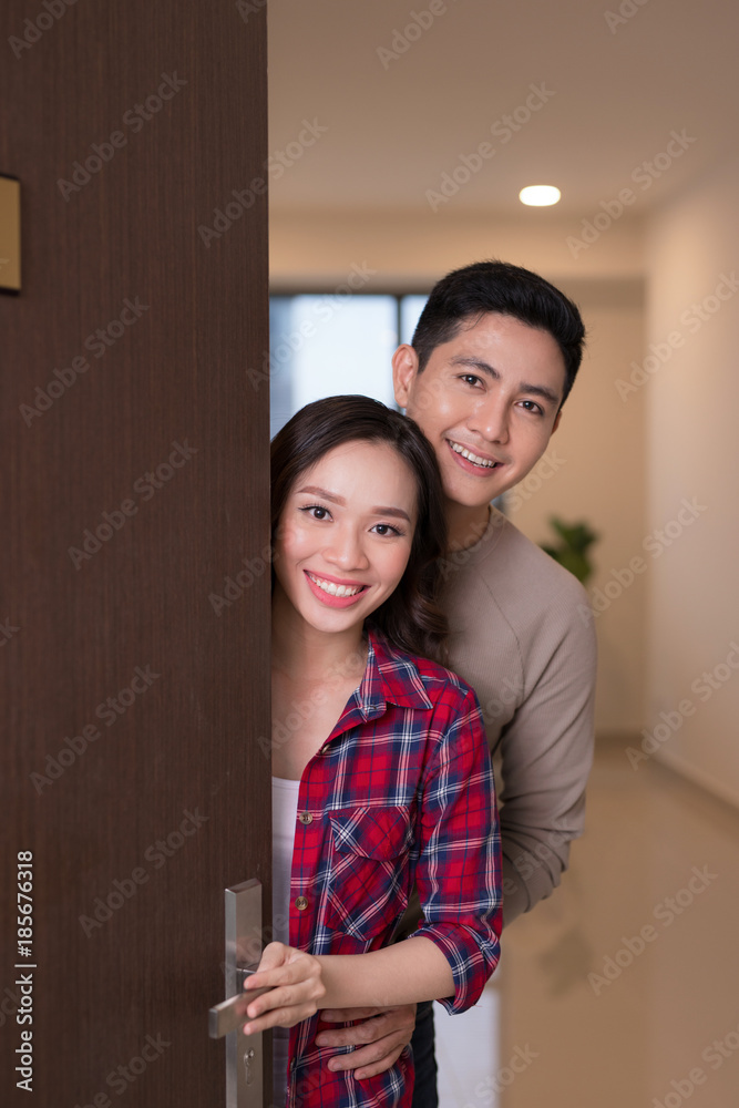 Cheerful young asian couple inviting people to enter in home