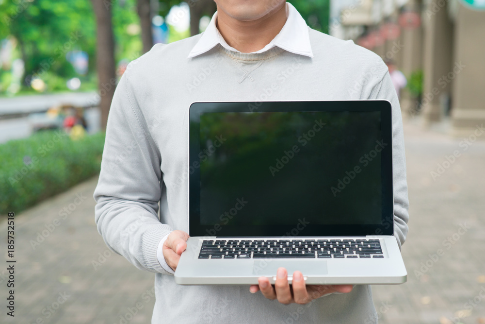 Young business man holding and showing the screen of laptop